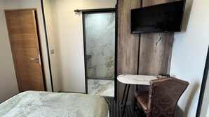 A hotel room with a bed, a small bathroom with a mirror and sink, and a television mounted on the wall. - Vrbo Property (Vicq-sur-Mer)