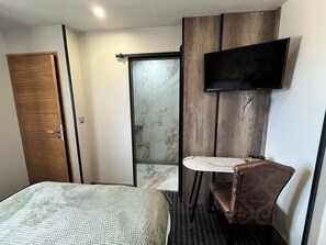 Ein Hotelzimmer mit Bett, einem kleinen Badezimmer mit Spiegel und Waschbecken sowie einem an der Wand befestigten Fernseher.