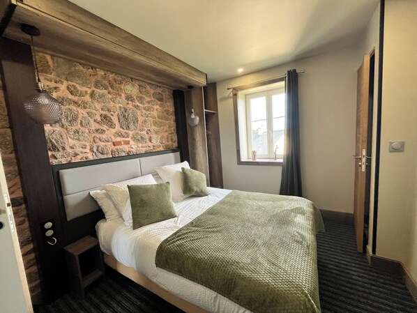 Ein Schlafzimmer mit einer Steinsäule, einem Bett mit weißer Bettwäsche und grünen Kissen, einem Fenster mit Vorhängen und einer Tür.