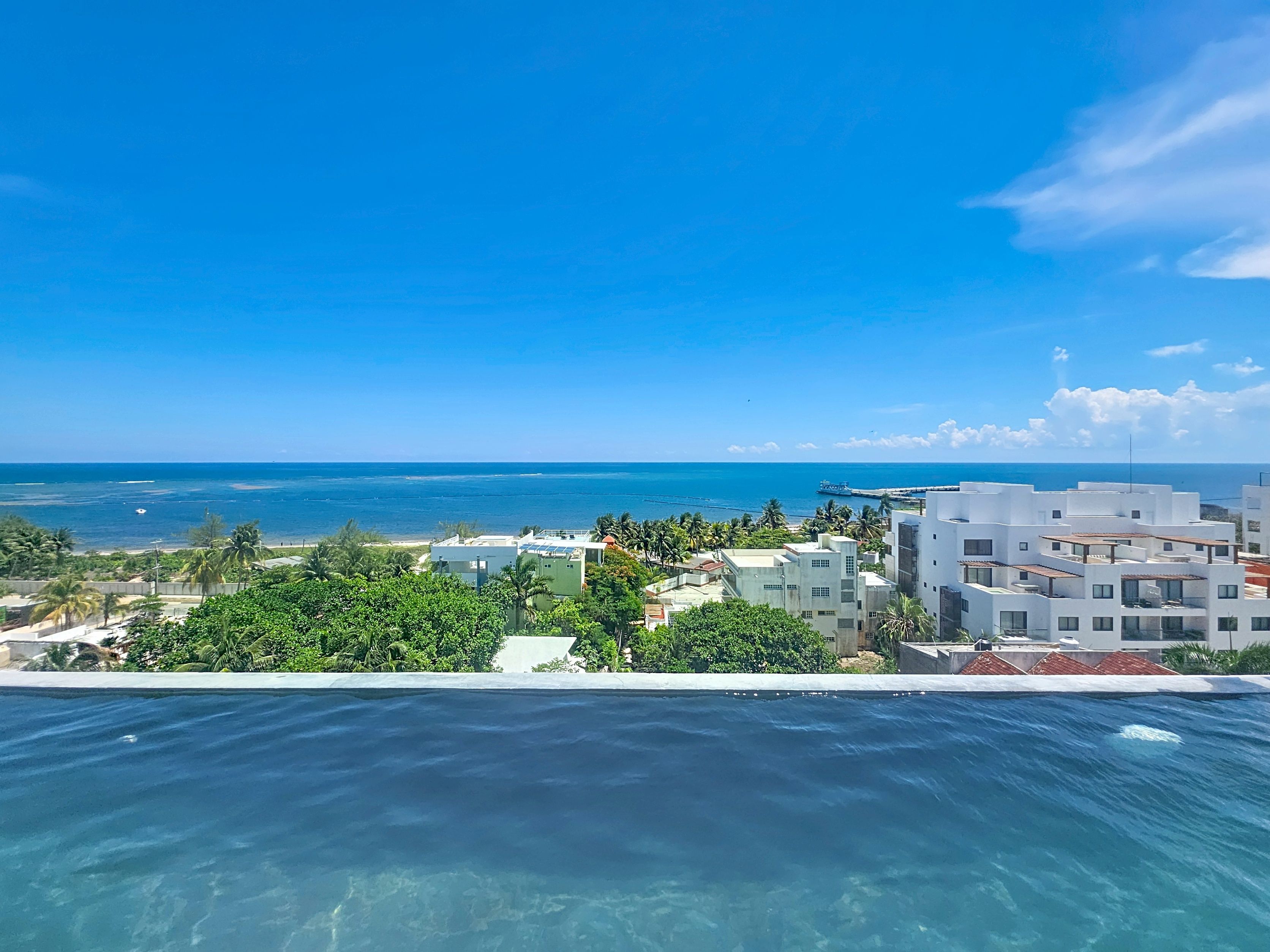 A clear view of a swimming pool with a backdrop of a coastal cityscape, including buildings and a distant view of the ocean.