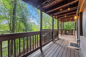 Eine Holzterrasse mit Geländer, umgeben von Bäumen, mit Lichterketten darüber.
