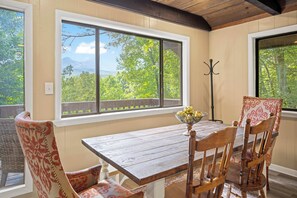 Ein Essbereich mit einem Holztisch und Stühlen, einem Fenster mit Blick auf Bäume und Berge sowie einem Kleiderständer.
