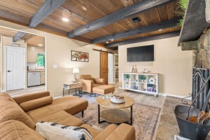 Ein geräumiges Wohnzimmer mit hohen Decken, Kamin, Fernseher und Essbereich, im Hintergrund eine Küche.