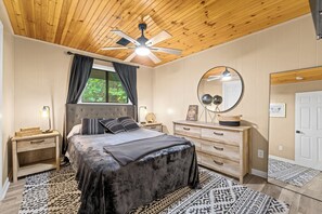 Ein Schlafzimmer mit Bett, Nachttisch, Kommode, Spiegel und Deckenventilator.