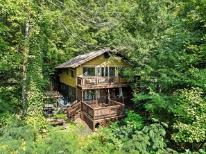 Een houten chalet met twee verdiepingen, omgeven door een dicht bos.