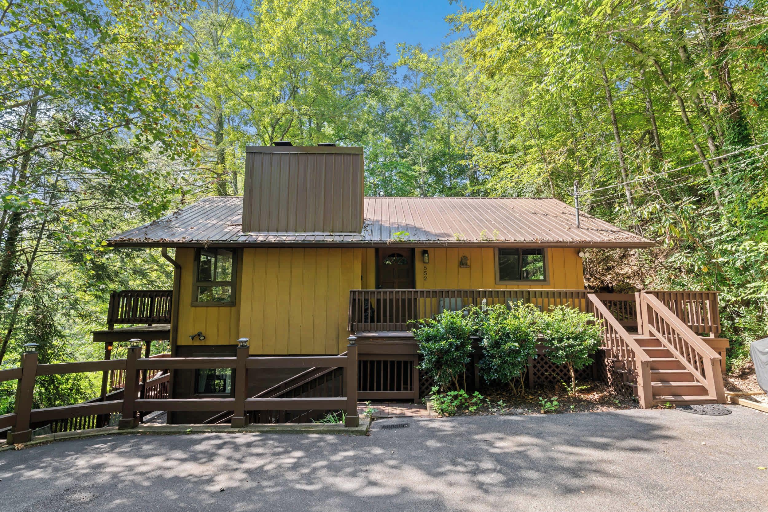 Ein gelbes Blockhaus mit Metall-Dach, Holzterrasse und einer Treppe zum Eingang.