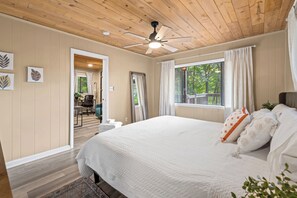 Een slaapkamer met een groot bed, een plafondventilator en een raam met gordijnen.