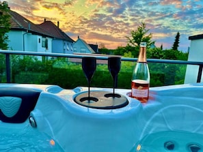 A hot tub with two wine glasses and a bottle of champagne, set against a sunset view.