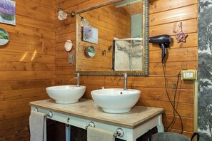 Ein Badezimmer mit Holzwandverkleidung, zwei weißen Waschbecken, einem Spiegel und einem an der Wand befestigten Föhn.