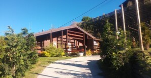 Une cabane en bois, accessible par un chemin de gravier, et entourée de verdure.