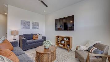 A modern living room with a grey sofa, a round coffee table, a wooden side table, a television mounted on the wall, and a ceiling fan.