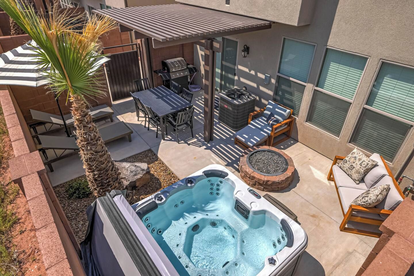 A backyard with a hot tub, patio furniture, a grill, and a palm tree.