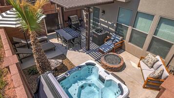 A backyard with a hot tub, patio furniture, a grill, and a palm tree.