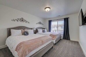 Een slaapkamer met twee bedden, een plafondlamp, een raam met gordijnen en een aan de muur bevestigde televisie.