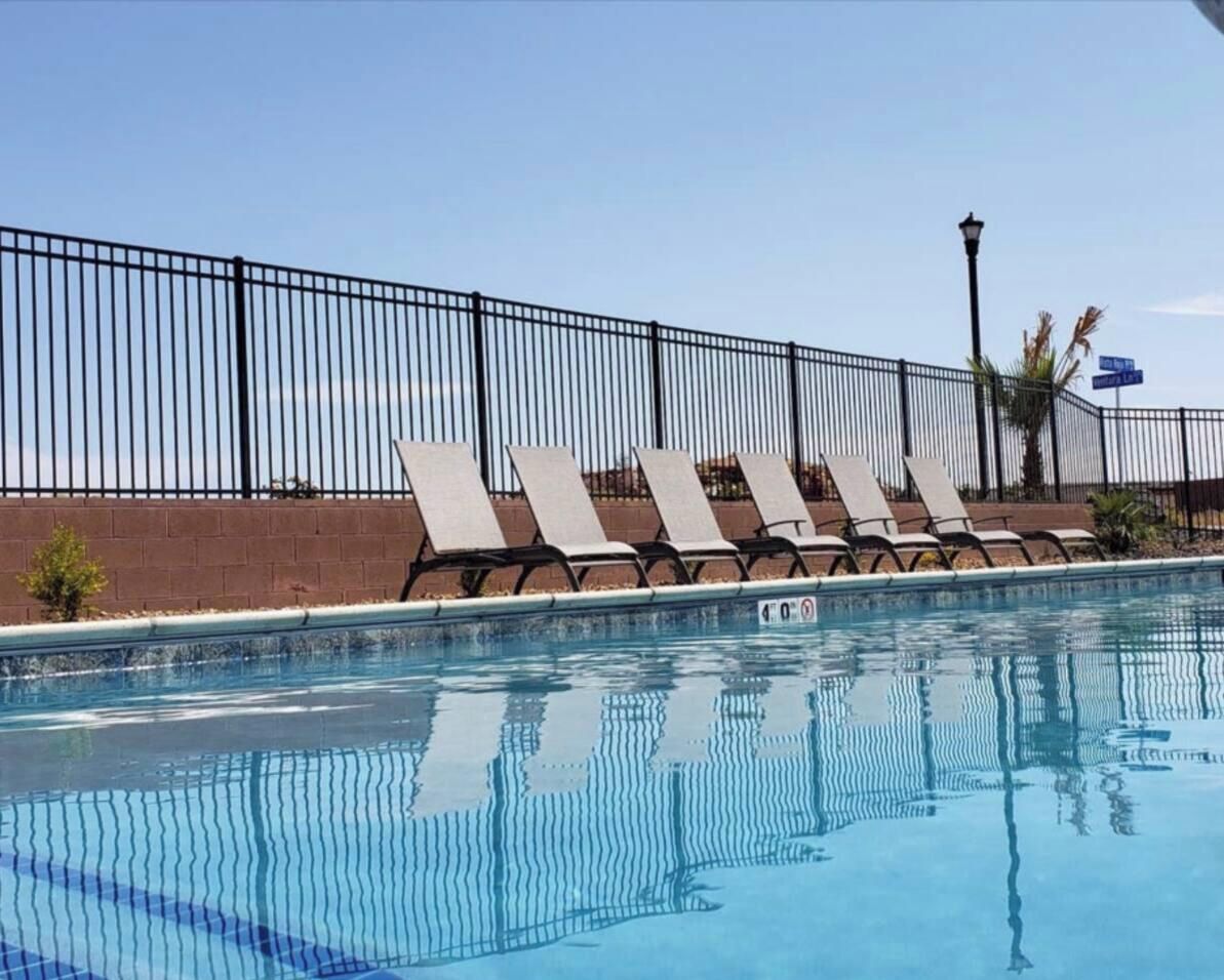 Piscina cercada por grade de metal preto, com espreguiçadeiras e céu claro.