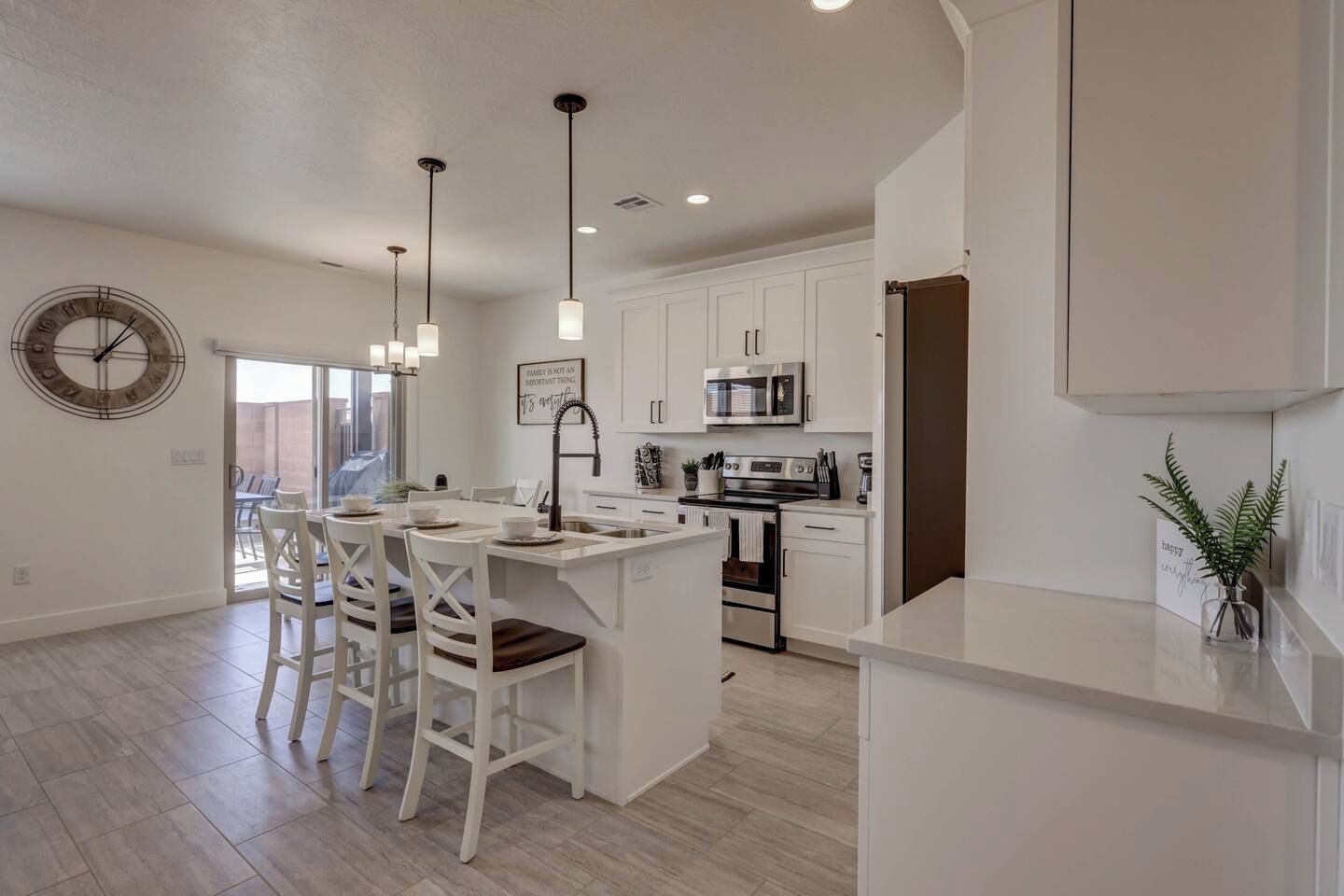 A modern kitchen with white cabinetry, a central island with bar stools, stainless steel appliances, and pendant lighting.