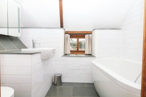 Ein modernes Badezimmer mit weißen Fliesen, einem Waschbecken, einer Toilette, einer Badewanne und einem Fenster mit Vorhängen.