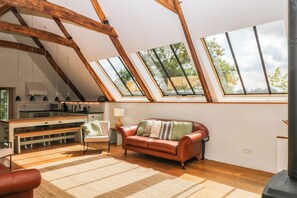 Ein Loft-Zimmer mit schräg verlaufender Decke, einer Couch, einem Couchtisch, einer Lampe und einer Küchenzeile.