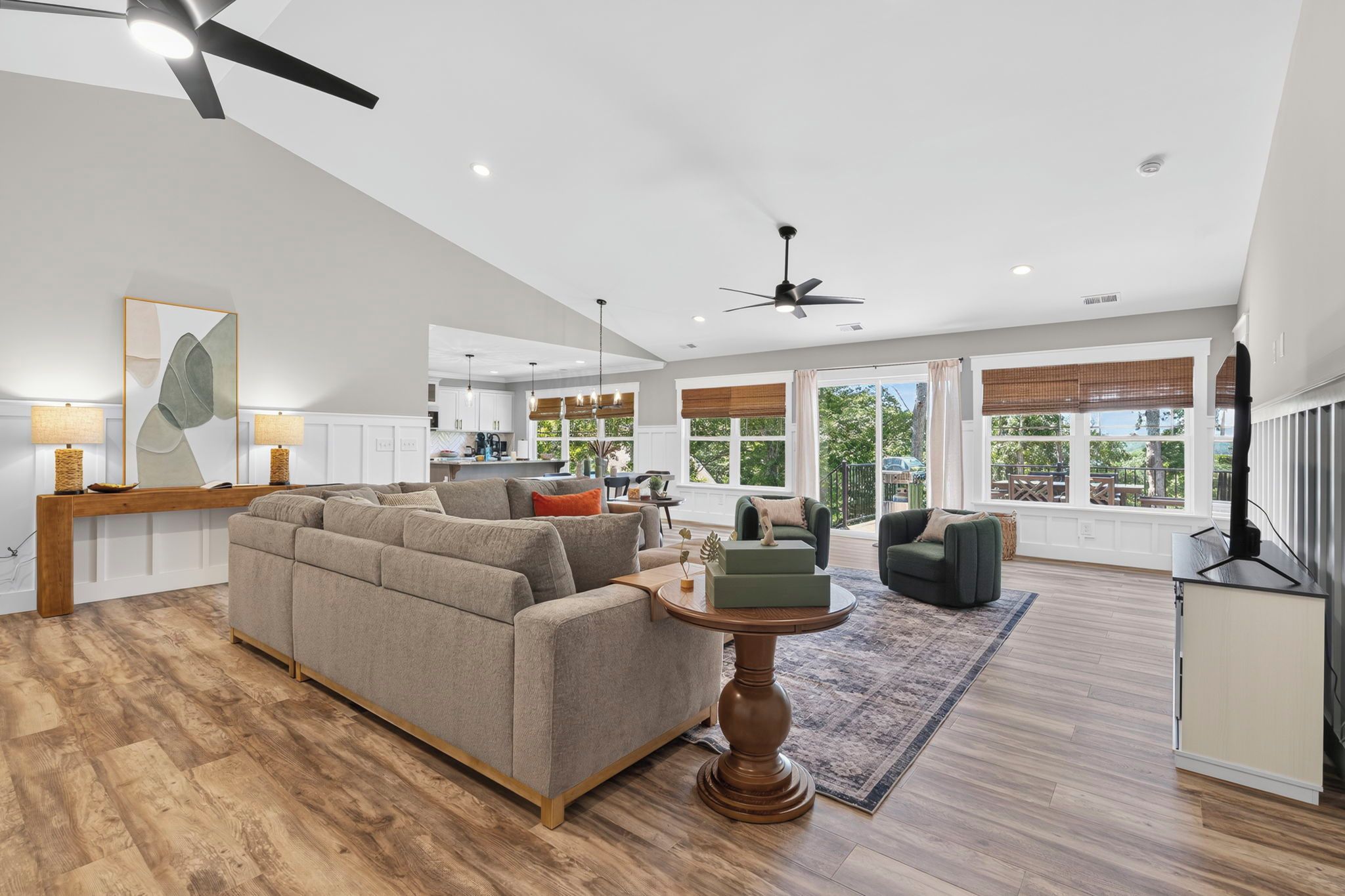 A spacious living room with a large sofa, a coffee table, and a television. There is a kitchen area visible in the background.
