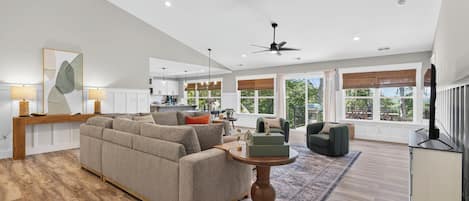 Amplia sala de estar con un sofá grande, una mesa de centro y un televisor. Se ve un área de cocina al fondo.