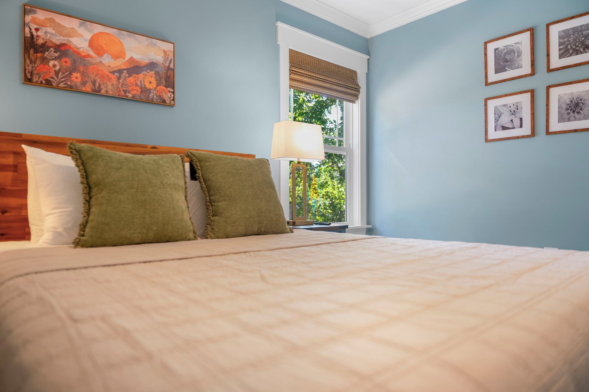 A bedroom with a bed, a window with a view, and a painting on the wall.