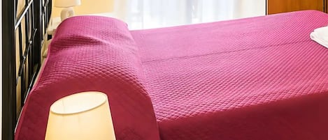 Una cama con un edredón rosa, una lámpara de noche y una puerta de madera al fondo.