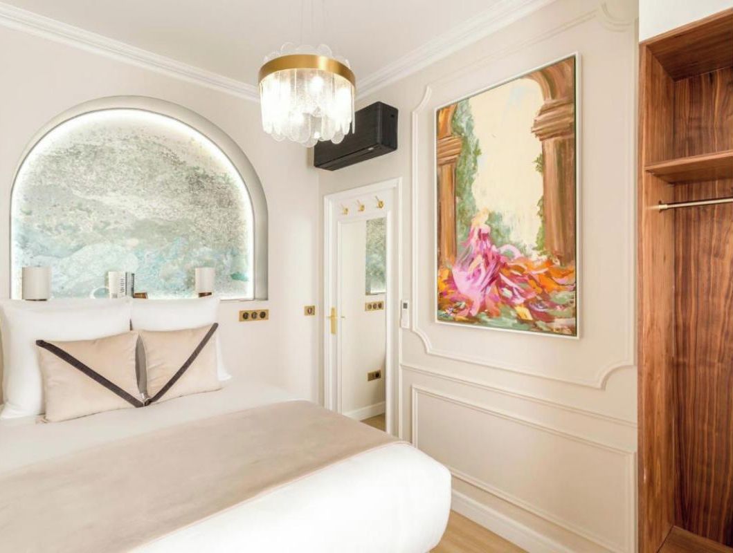 Une chambre à coucher avec un grand lit, un miroir rond, un lustre, un tableau et une armoire en bois.