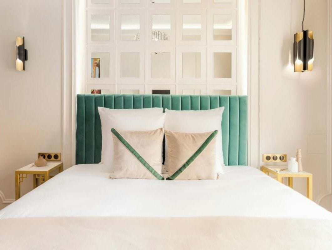 Un letto con una testiera color petrolio, due cuscini bianchi e una coperta bianca.