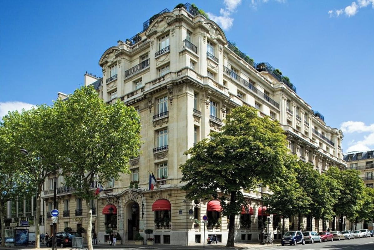 Een meerlaags hotel met een klassieke architectuur, met balkons en een centrale ingang met een rode luifel.