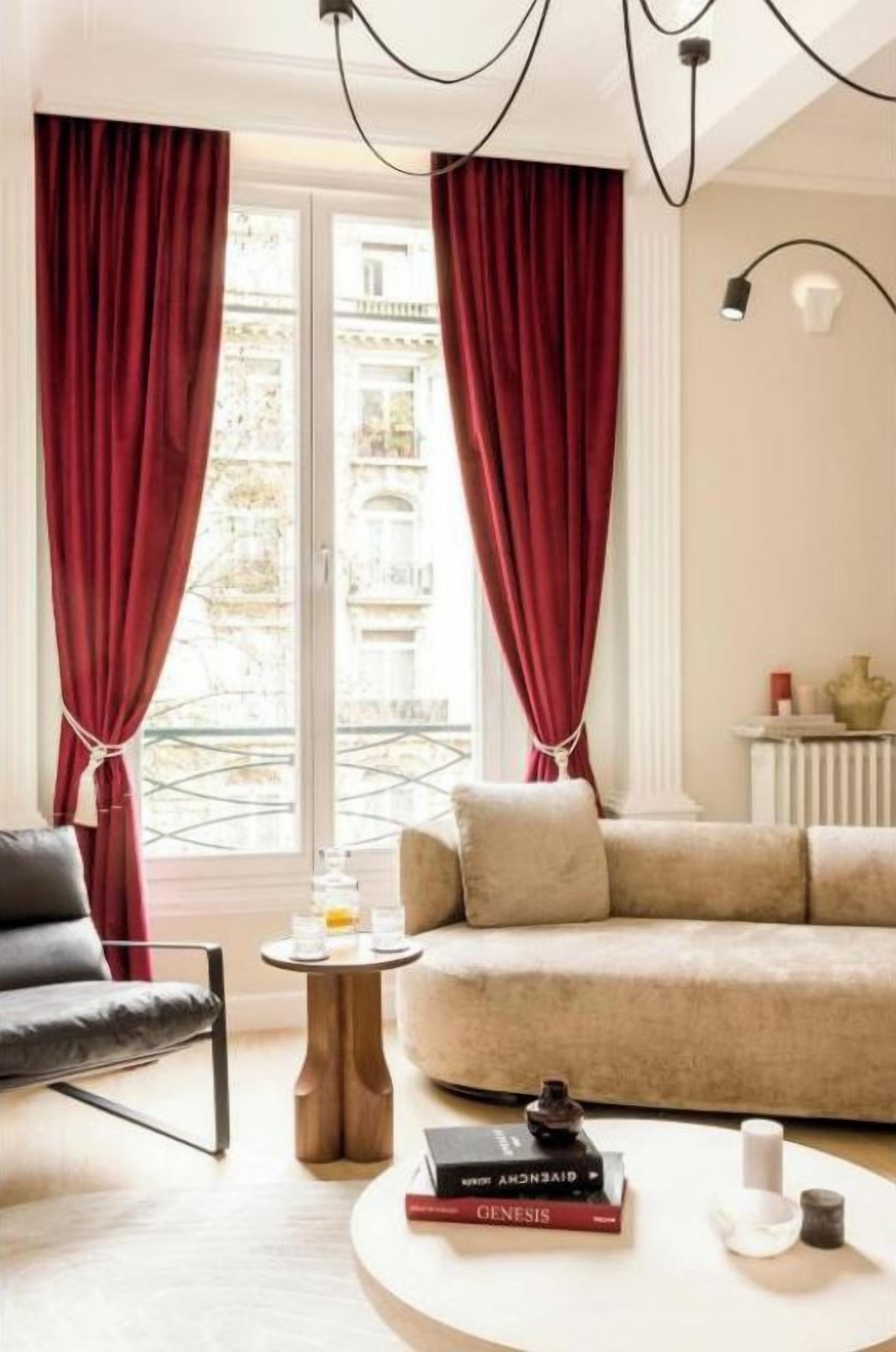 Sala de estar com sofá, mesa de centro e uma poltrona. Há uma janela com cortinas, um radiador e um abajur.
