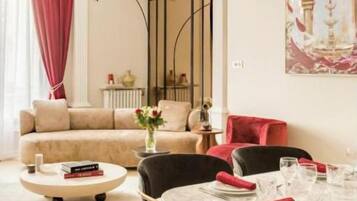 Uma área de refeições com mesa posta para quatro pessoas, um sofá ao fundo e um quadro na parede.