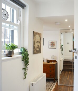 Um corredor com radiador, cômoda de madeira, planta em vaso e porta que dá para outro quarto.