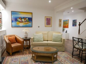Uma sala de estar com sofá, poltrona, mesa de centro e um quadro na parede.