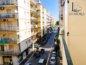 A multi-story residential building with balconies, a street in front, and parked cars.