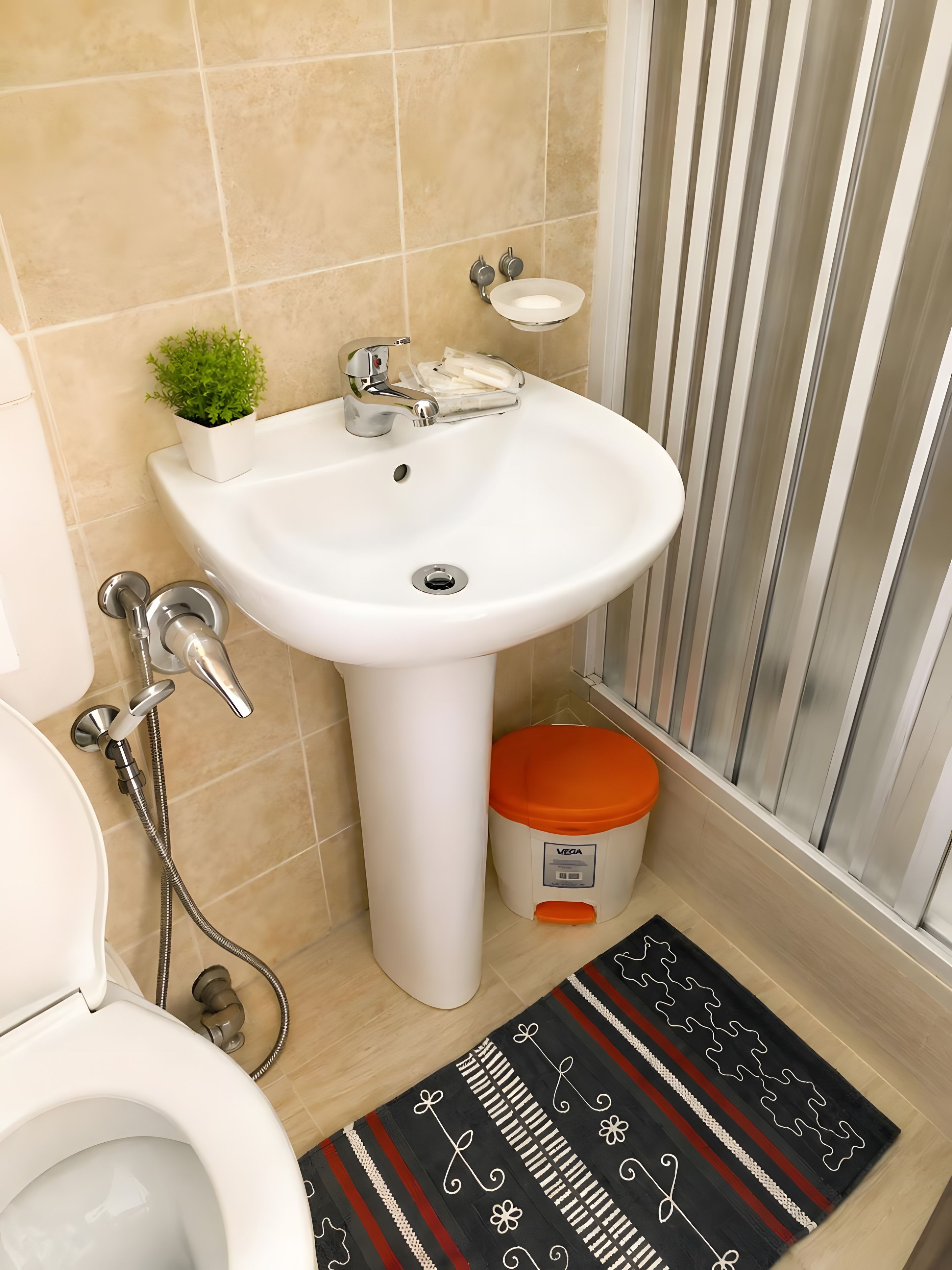 Une salle de bain avec un lavabo blanc, une petite plante en pot, des toilettes et un espace douche.