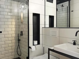 Un baño moderno con azulejos blancos tipo metro, un lavamanos con marco negro y una ducha con cerramiento de vidrio.