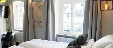 A hotel room with a bed, a desk, a chair, and a large window.