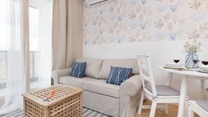 Ein Wohnzimmer mit einer Couch, einem Esstisch mit Stühlen, einem kleinen Holztisch und einem Fenster mit transparenten Vorhängen.