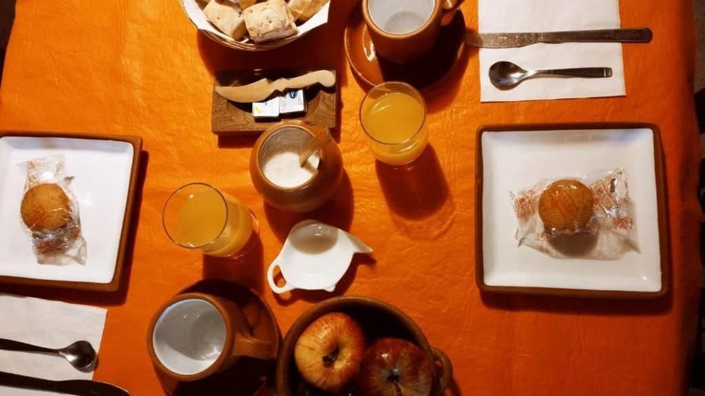 Desayuno servido con platos de comida, tazas y un bol sobre un mantel naranja.