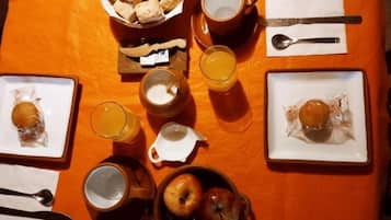 Desayuno servido con platos de comida, tazas y un bol sobre un mantel naranja.
