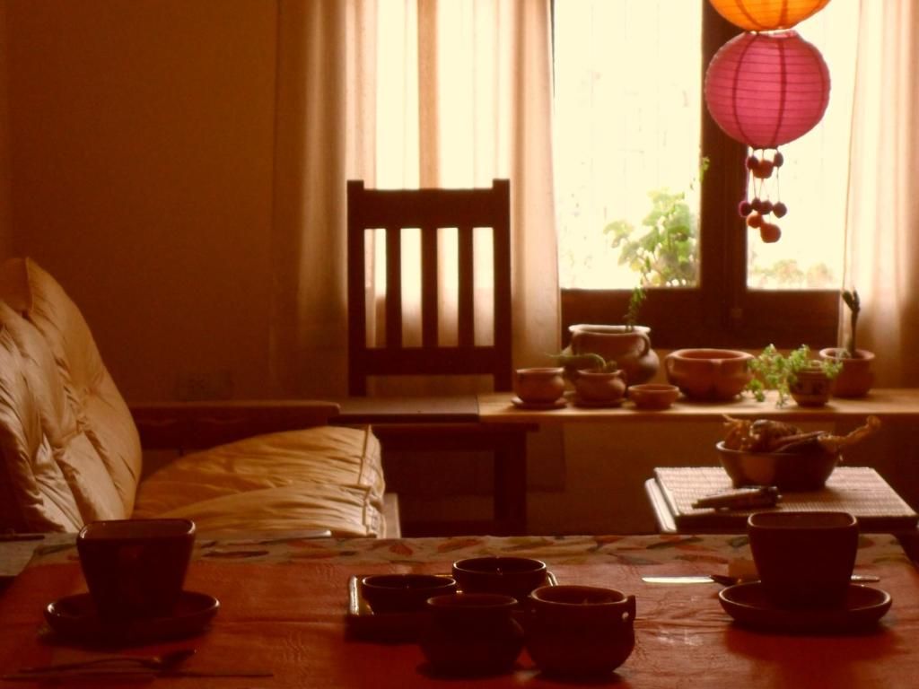 Una habitación con una cama, una mesa con tazas y platos, una silla y una ventana con cortinas.