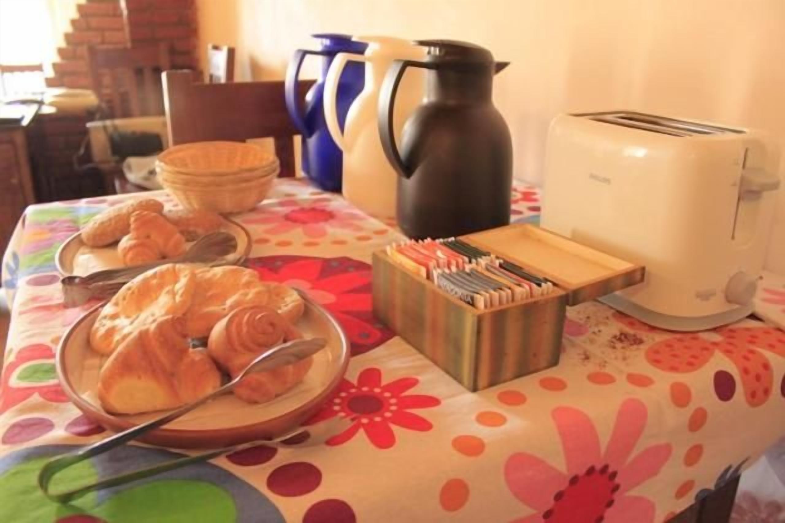 Una mesa de desayuno con cruasanes, una cafetera, un tostador y un juego de cubiertos.