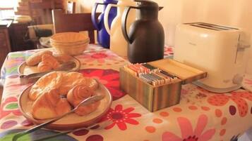 Una mesa de desayuno con cruasanes, una cafetera, un tostador y un juego de cubiertos.