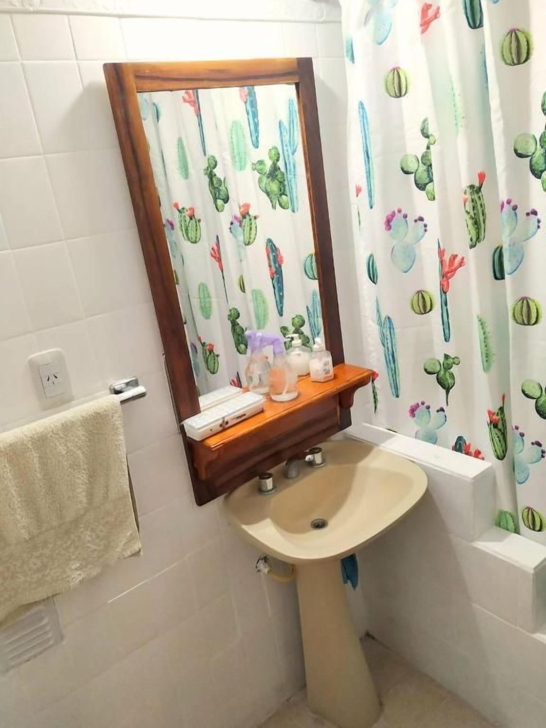 Un baño con lavamanos, espejo y cortina de ducha con estampado de cactus.