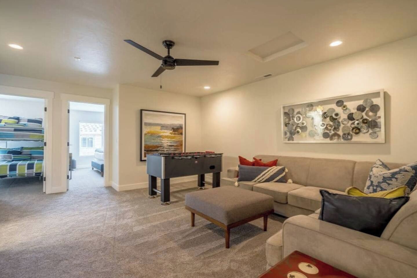 A living room with a sofa, ottoman, foosball table, and a ceiling fan.