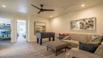 A living room with a sofa, ottoman, foosball table, and a ceiling fan.