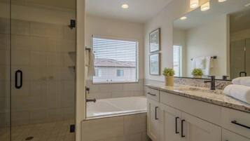 A bathroom with a walk-in shower, a bathtub, a large mirror, and a countertop with a plant.