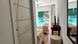 A hotel room with a large mirror, two beds, a small seating area, and a view of a pool. - Pousada M&M (Petrópolis)