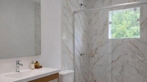 A modern bathroom with a marble wall, a glass shower enclosure, and a large mirror. - Pousada M&M (Petrópolis)