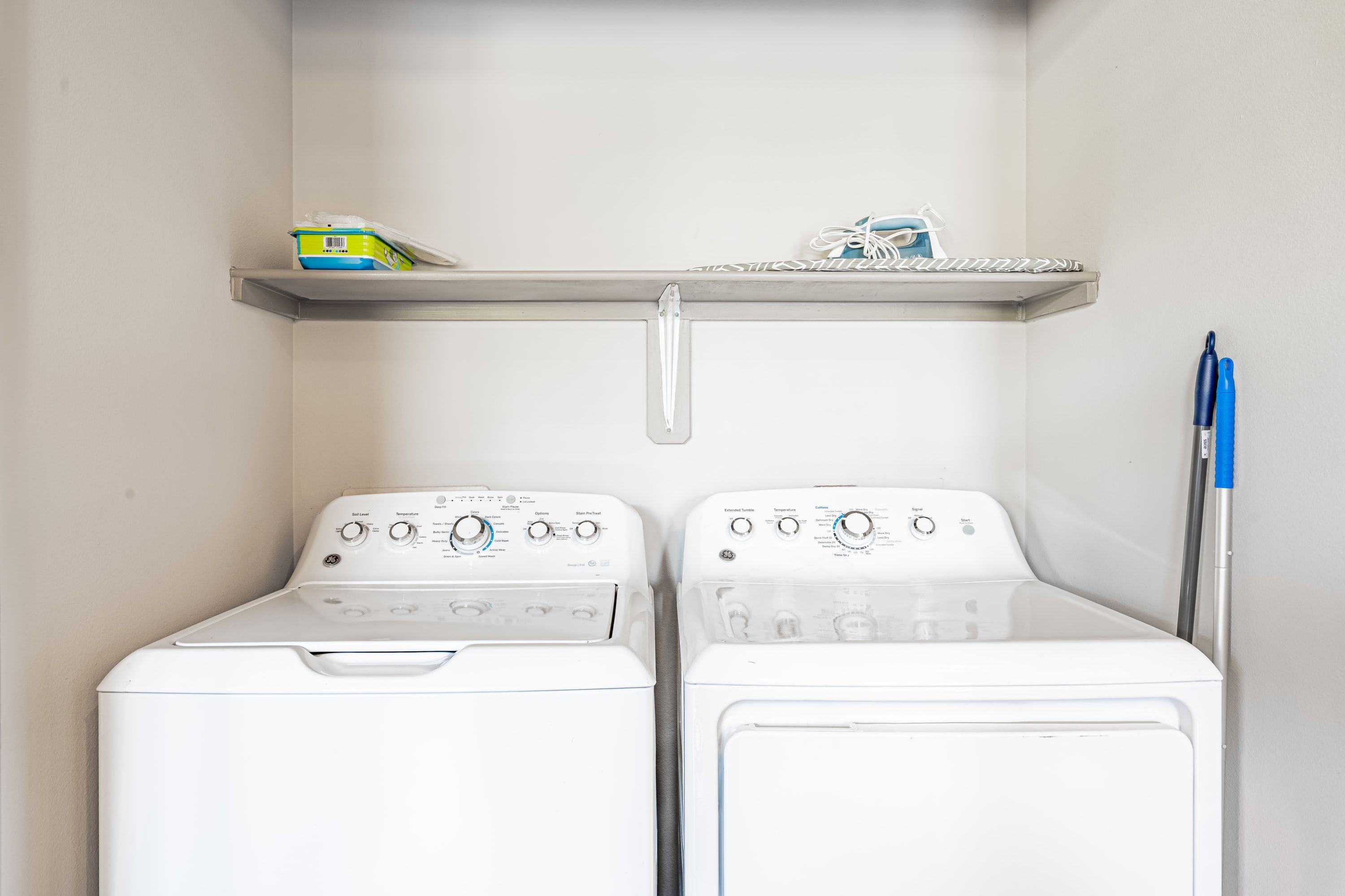 A laundry area with two front-loading washing machines and a shelf above them.
